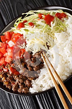 Takoraisu Okinawan Taco Rice with ground beef, vegetables, cheese and sauce close-up in a bowl. vertical