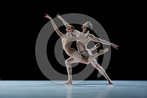 Talented, artistic young couple, man and woman, ballet dancers making impressive performance against black studio