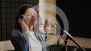 Talented Asian Female Singer Wearing Headphones Singing Song To Mic In Studio
