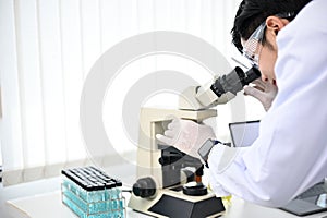 Talented Asian male scientist or chemist looking under the Microscope, working in the lab