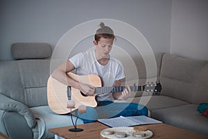Talented boy playing a wooden acoustic guitar in a lighted room. Blonde Man aged 20-29 strums guitar and sings from hymn book on