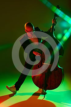 Talented cellist performing jazz compositions in red-green neon light against gradient studio background.