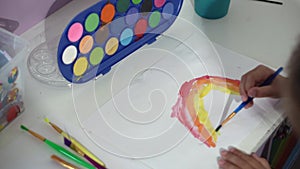 Talented creative child girl female artist draws rainbow sky summer on paper, using fingers paints brush creates