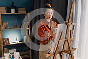 Talented female painter in home studio. Young artist working painting on a canvas with a paintbrush and holding a color