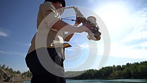 Talented jazz musician is playing saxophone at nature at summer day, man is blowing into sax