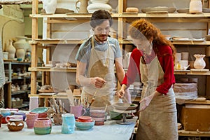 Talented long-haired woman in apron using paintbrush for decorating