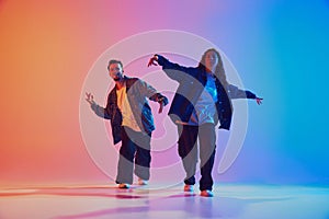 Talented male and female hip-hop dancers performing in synchronously moves against gradient studio background in neon