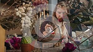 Talented woman surrounded by beautiful flowers in her studio creates a unique floral arrangement by covering the surface