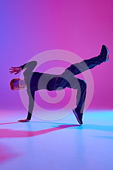 Talented young boy in black attire, street dancer performing tricks in mid-air in mixed neon light against vibrant