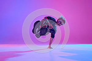 Talented young boy, street dancer performing breakdance tricks in mid-air in mixed neon light against vibrant gradient