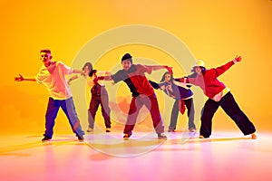 Talented young dancers performing streetstyle dance in motion in neon light against gradient colorful studio background.