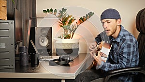 Talented young guy singing song and playing acoustic guitar. Musician playing acoustic guitar, enjoying leisure time in apartment.