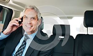 Talking business on the way to work. a mature businessman using a mobile phone in the back seat of a car.