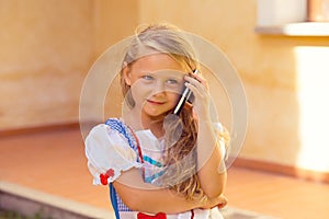 Talking with parents. Happy little girl kid outside near her house listens to what he`s talking on the phone speaking on the