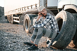 Talking by phone. Young truck driver is with his vehicle at daytime