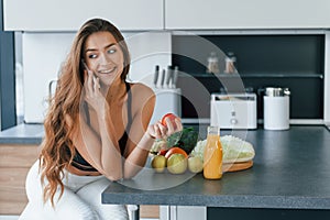Talks by the phone. Young european woman is indoors at kitchen indoors with healthy food