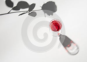 Tall art deco glass with red liquid, rose shadow against bright background