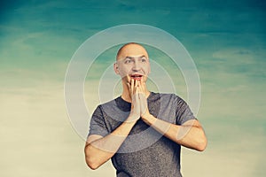A tall bald man in a gray T-shirt covered his surprised face with his hands