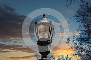 A tall black lamp post surrounded by bare winter trees with blue sky and powerful clouds at sunset in the Marietta Square