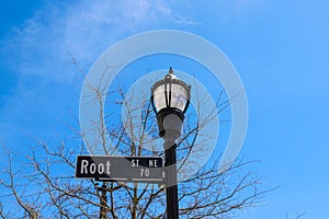 A tall black metal lamp post with street signs surrounded by bare winter trees with blue sky and clouds in the Marietta Square