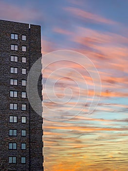 Tall brown brick skyscraper residential building with many windows against sunset sky.