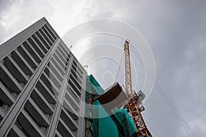 Tall building with tower crane view from ground. Green shade cloth over grey concrete building. Modern construction site