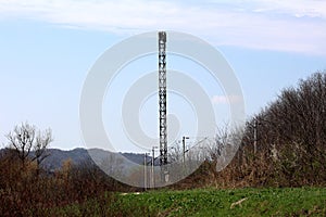 Tall cell phone metal antenna tower next to railroad with multiple electrical poles surrounded with uncut green grass and dense