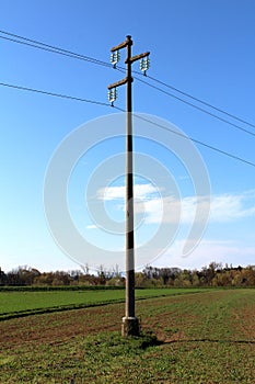 Tall concrete power line utility pole with glass insulators holding electrical wires in middle of field surrounded with grass and