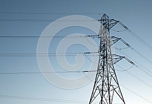 Tall electricity pylon with multiple high voltage cables silhouetted against a blue sky