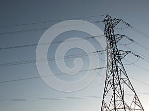 Tall electricity pylon with multiple high voltage cables silhouetted against a blue sky