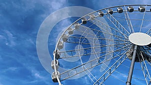 A tall Ferris wheel with closed booths slowly rises against the blue sky