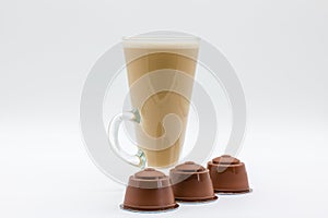A tall glass of coffee latte or cappuccino and three generic coffee pods