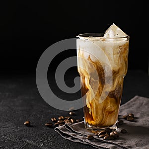 Tall glass cold brew coffee with ice and milk on black or dark b