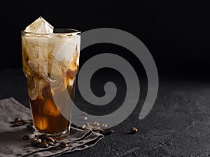 Tall glass cold brew coffee with ice and milk on black or dark b