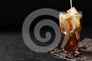 Tall glass cold brew coffee with ice and milk on black or dark b