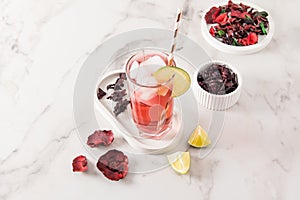 A tall glass of cold tea made of hibiscus rose petals on a plaster tray and marble table. a cooling thirst-quenching drink in hot