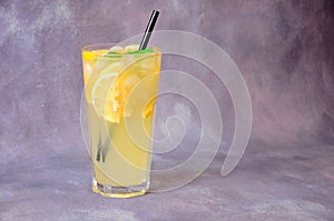 Tall glass cup of lemon mojito with ice, mint leaves and slices of citrus on a gray background