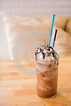 Tall glass of delicious cold iced coffee float or milkshake topped with ice cream or cream on a rustic wooden counter for