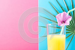 Tall Glass with Freshly Squeezed Pineapple Citrus Tropical Fruit Juice with Straw and Flower. Pink and Blue Background Palm Leaf