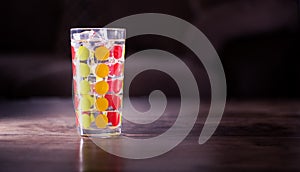 Tall glass with green, orange and red dots filled with ice cubes and lemonade isolated on dark background