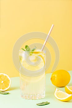 Tall glass of ice tea or water with ice cubes, lemon and mint leaves on a combined colored yellow and green background