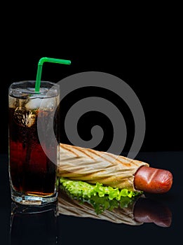 Tall glass of iced coke with a hot dog