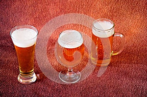 Tall glass, mug and glass with light beer with white foam on a brown background