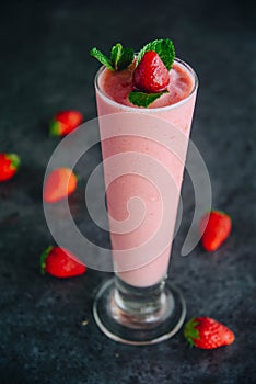 A tall glass with pink drinks or beverages from juicy and fresh red strawberries