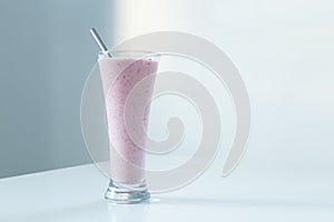 Tall glass with strawberry smoothie and stainless steel straw set in natural light