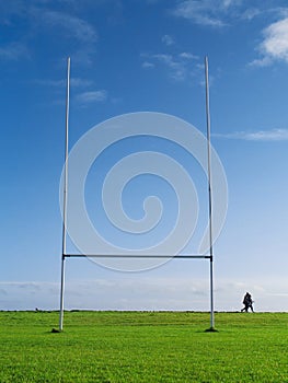 Tall goal post for Irish National sport rugby, hurling, gaelic football and camogie on a green training pitch, blue cloudy sky.