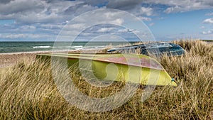 Tall grass at the beach, Green and blue boats lying in the grass with the bottom up. The sea in the background. blue sky with