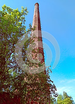Tall hexagonal brick pipe on a sunny summer day among foliage against a blue sky