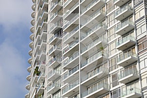 A tall high rise apartment building with balconies against a light blue sky backdrop