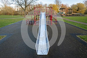 Tall, high, skinny, stainless steel silver slide coming off metal play structure in children's playground.